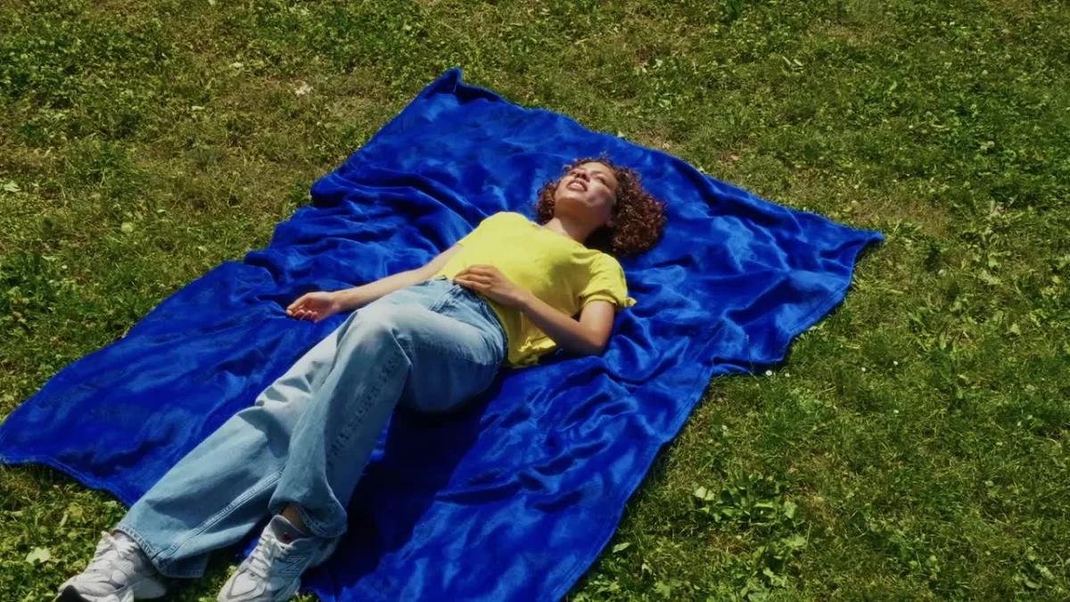 Junge Person liegt auf einer blauen Decke im Gras